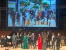 All of the gala's performers gather on stage, under a projected photo of 				the groundbreaking for the new building